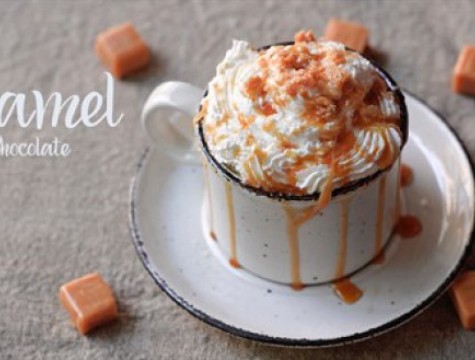 Cup of salted caramel hot chocolate with whipped cream sitting on a matching saucer.